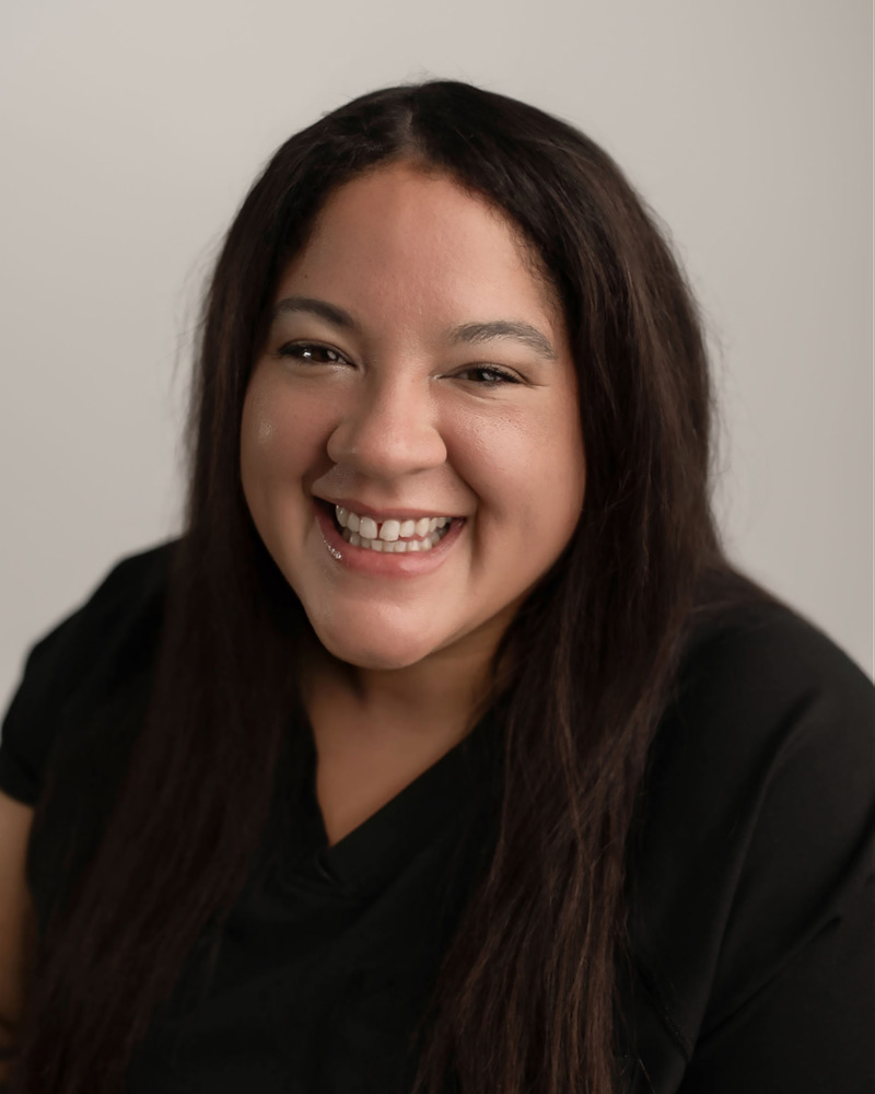 Lindsey, registered dental assistant, smiling warmly in black scrubs against a neutral background